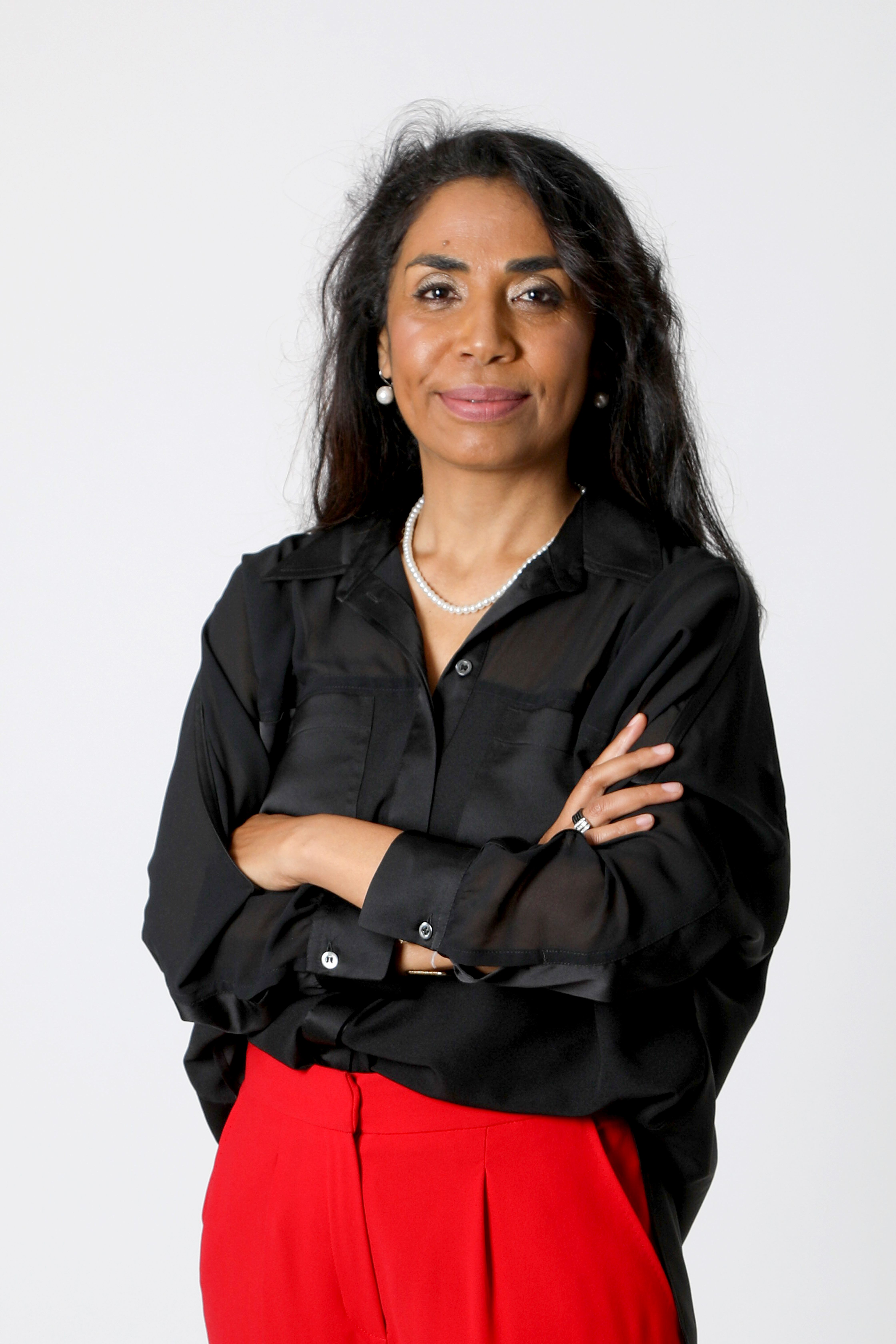 Portrait professionnel du Dr Joéline Andriana, Docteur en Psychologie Sociale. Elle porte une chemise noire et un pantalon rouge, posant avec assurance sur un fond blanc. Experte en accompagnement du changement, leadership et résilience pour les dirigeants et particuliers.