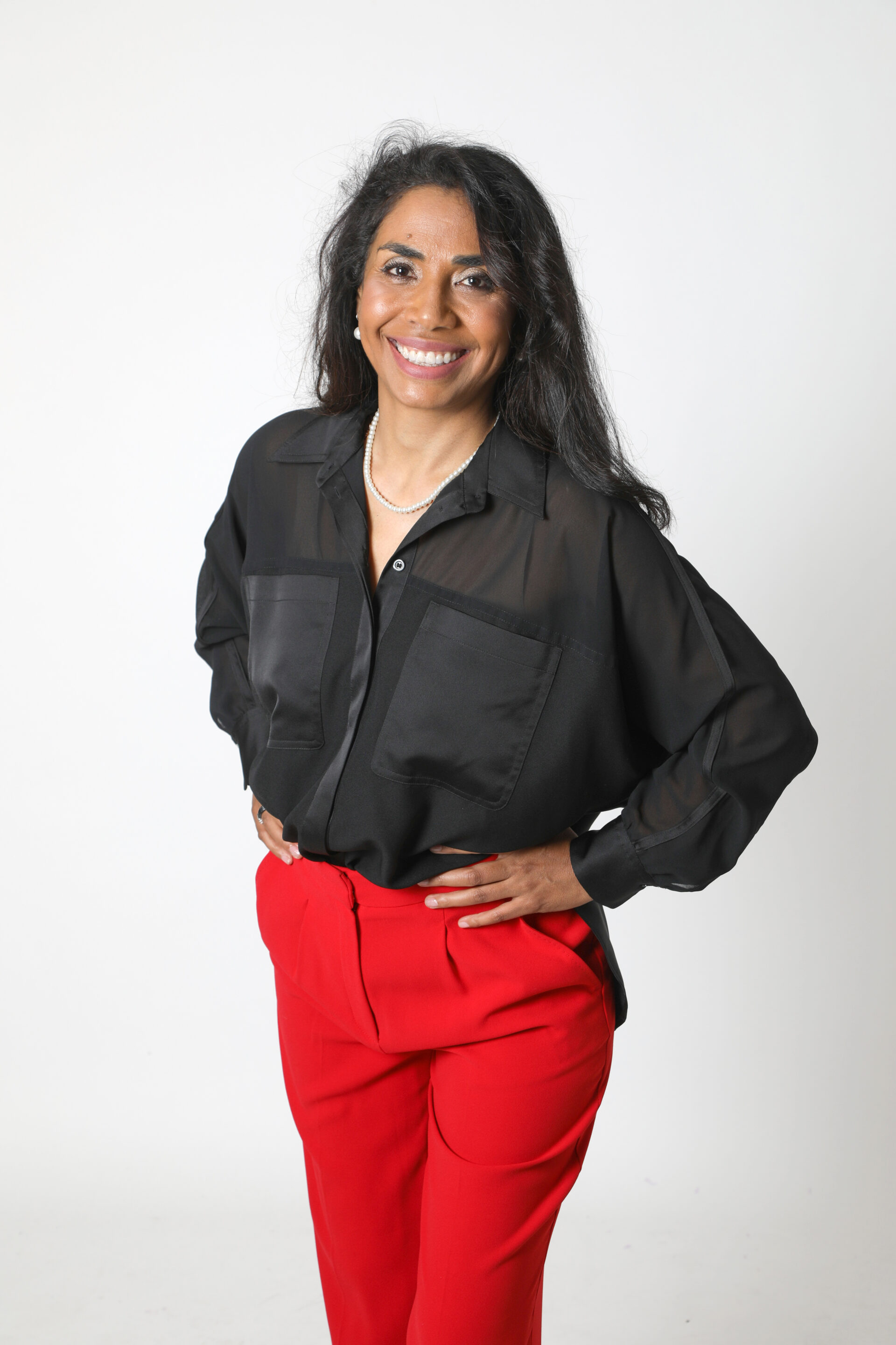 Portrait du Dr Joéline Andriana, Docteur en Psychologie Sociale et auteure, pour sa page de publications et pensée stratégique. Elle pose avec assurance en chemisier noir et pantalon rouge, incarnant la rigueur intellectuelle et la créativité nécessaires à ses travaux de recherche, ses essais et ses ouvrages sur l'humain et l'organisation.